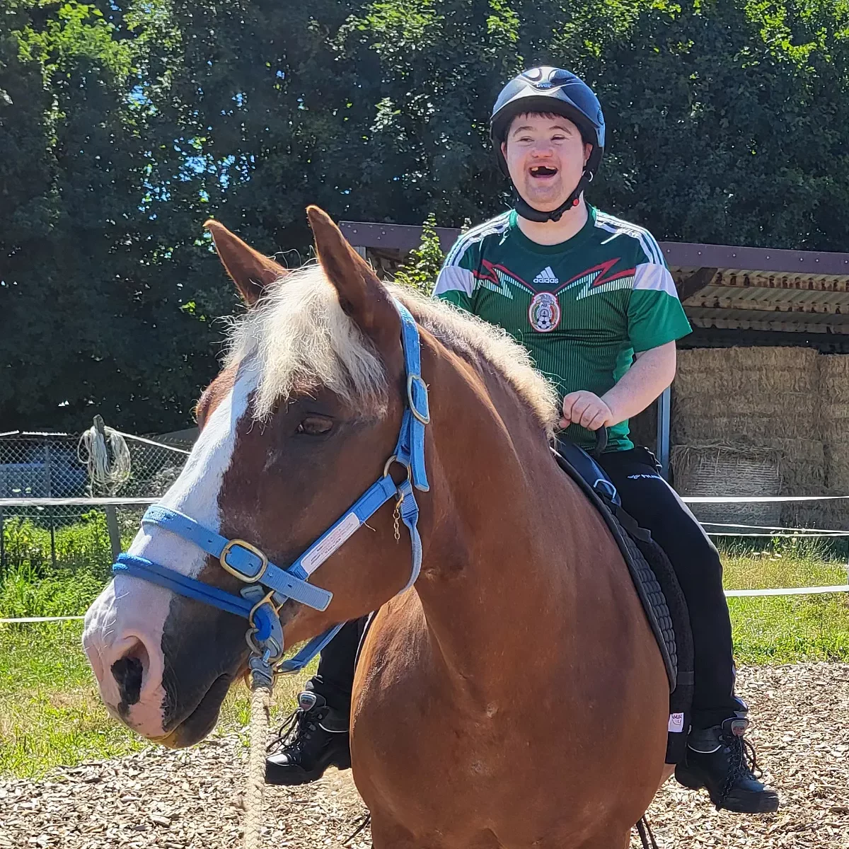Junger Mann mit Downsyndrom sitzt bei der Reittherapie auf einem Pferd und lacht.